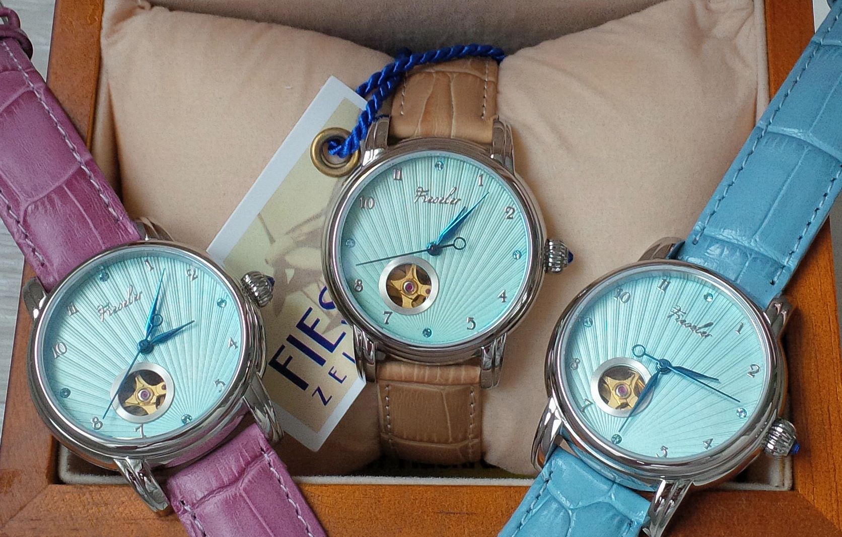 Drei Uhren mit blauen, pinken und braunen Armbändern in einer schwarzen Box